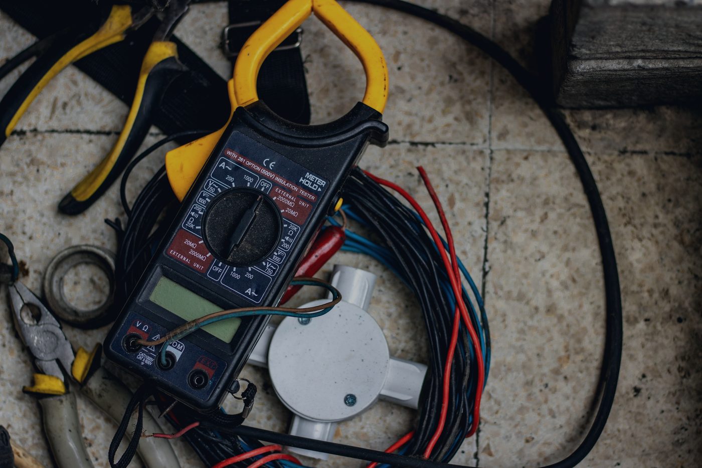 A clamp meter and test leads resting on electrical cables