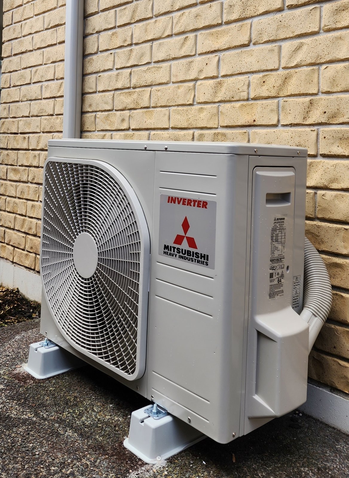 A Mitsubishi Heavy Industries inverter heat pump outdoor unit installed on feet against a brick wall